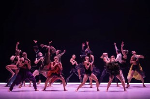 Dancers on stage mid-performance with purple down lights and abstract costumes.